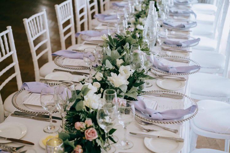 A long table with plates , glasses , napkins and flowers .