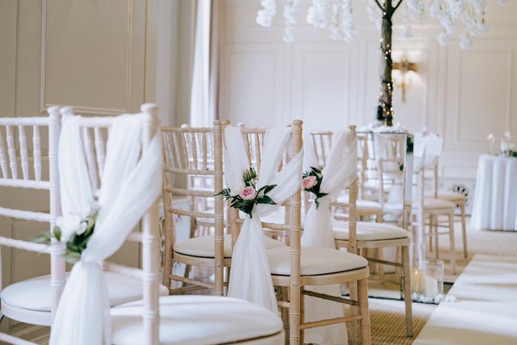 The chairs are decorated with flowers and tulle and are lined up in a row .