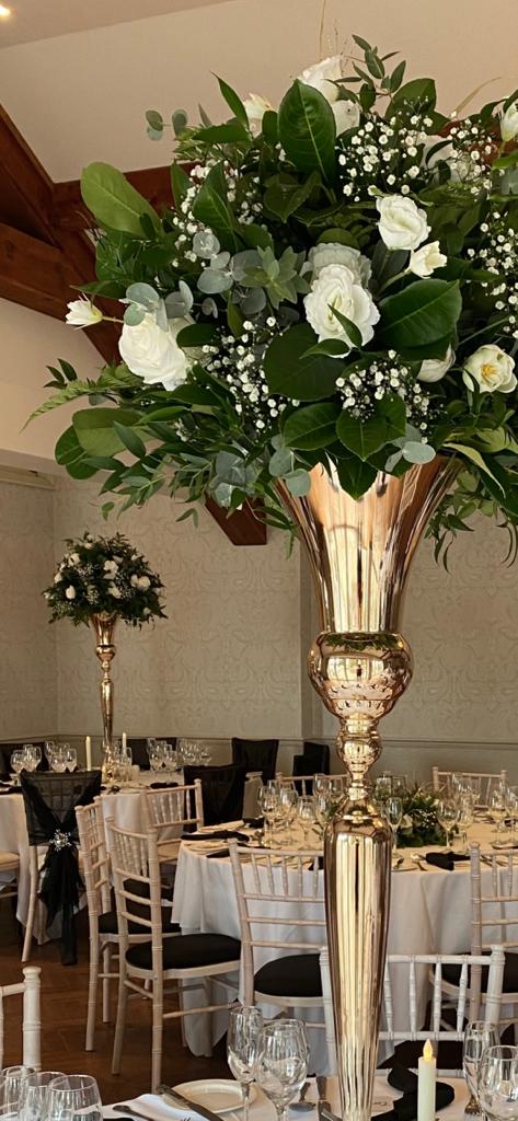A large gold vase filled with white flowers and green leaves