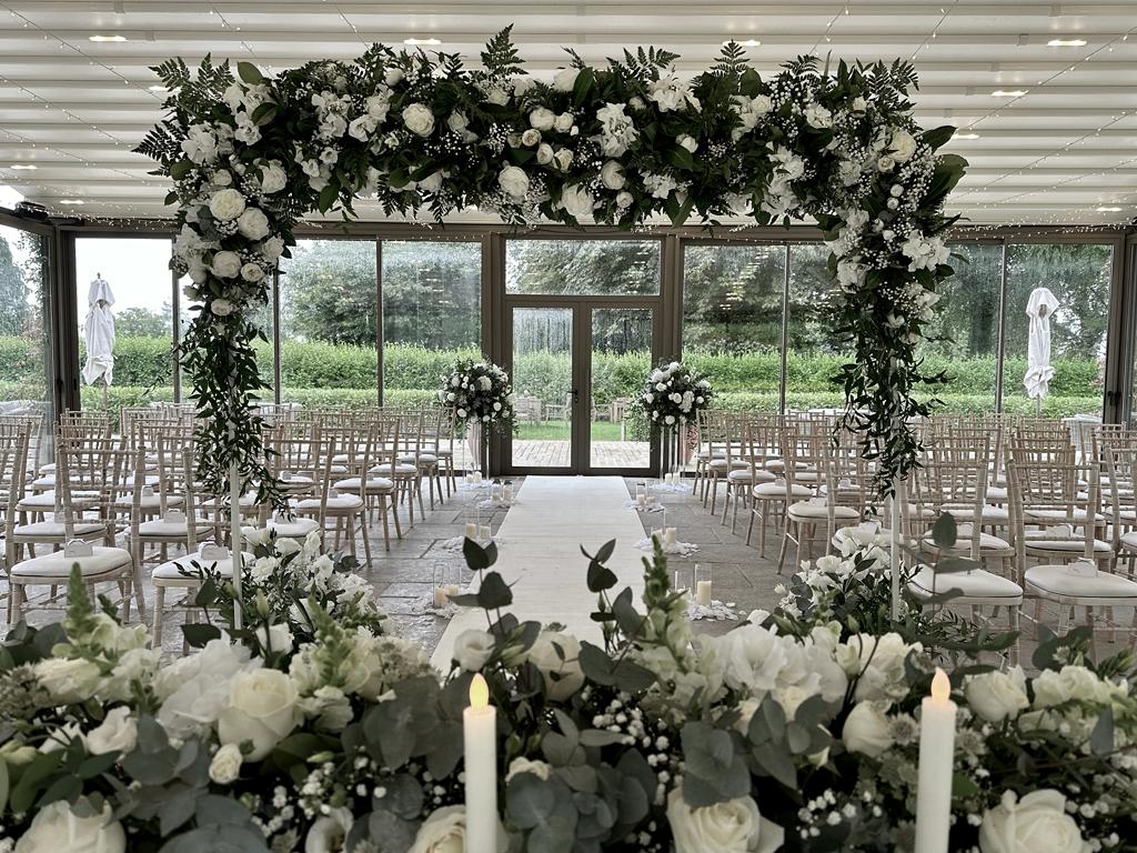 A wedding ceremony is taking place in a room with white chairs and candles