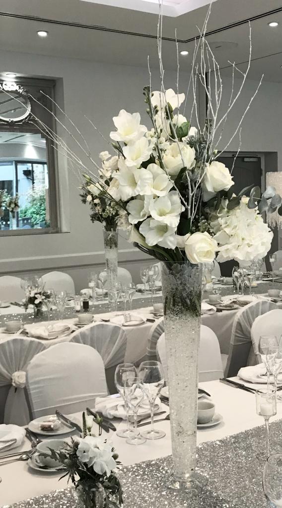 A table set for a wedding reception with white flowers in tall vases