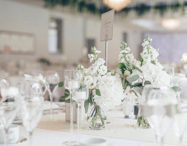 A table set for a wedding reception with white flowers in vases and wine glasses .