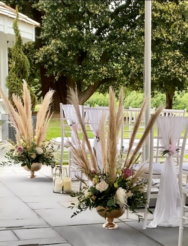 A row of chairs are decorated with flowers and pampas grass