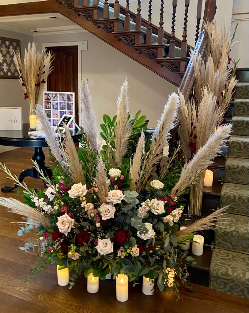 A large display of flowers and candles in front of a wooden staircase