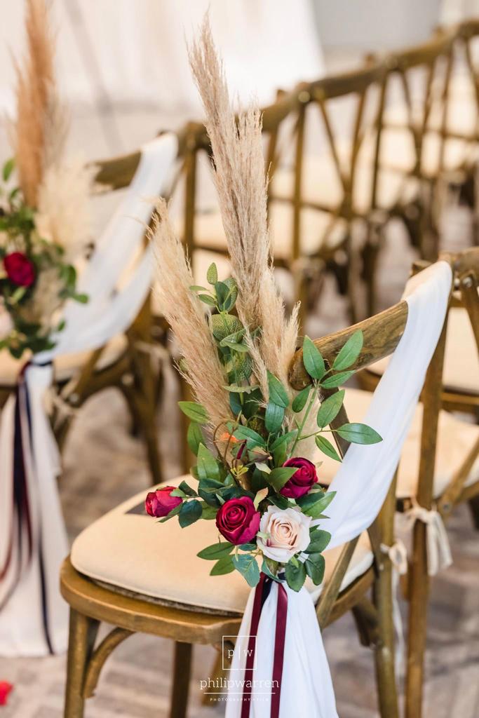 A row of chairs decorated with flowers and pampas grass