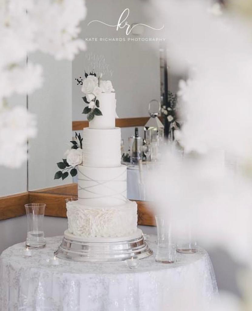 A white wedding cake sits on a table in front of a mirror