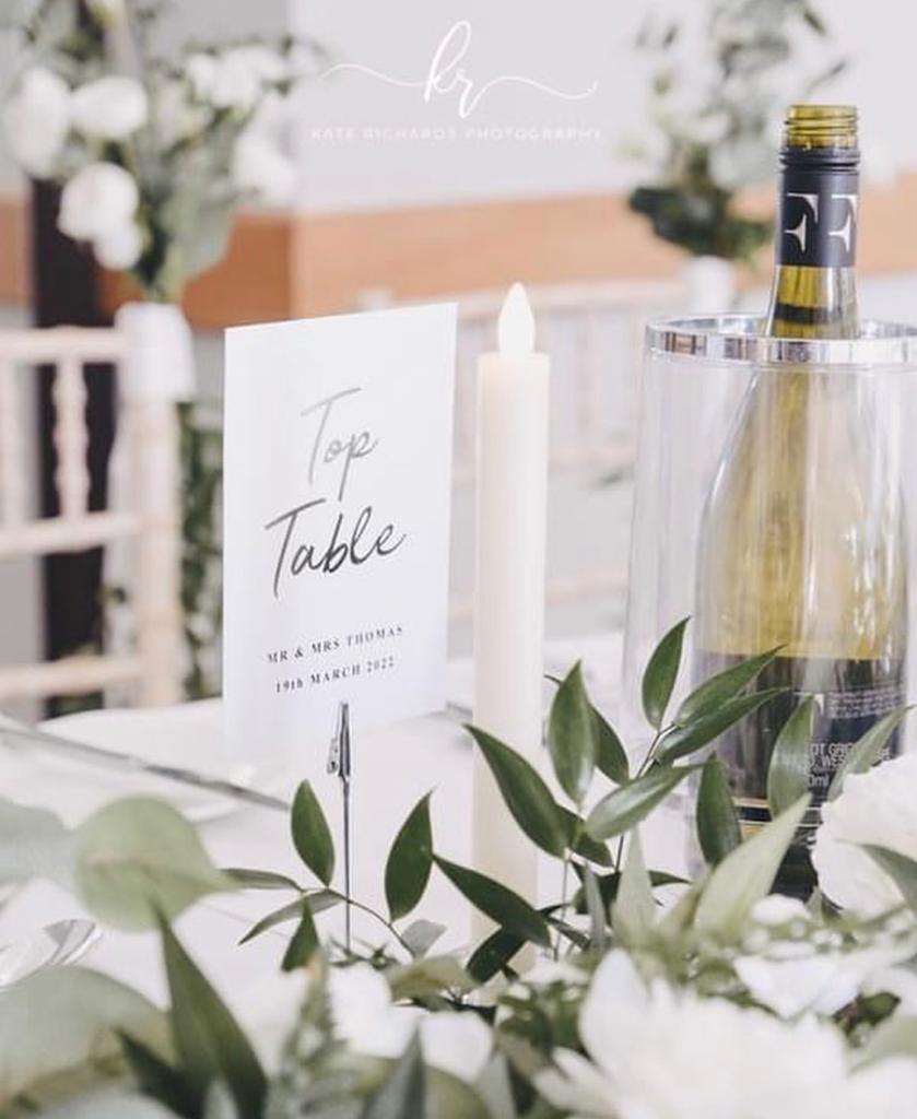 A bottle of wine sits on a table next to a sign that says top table