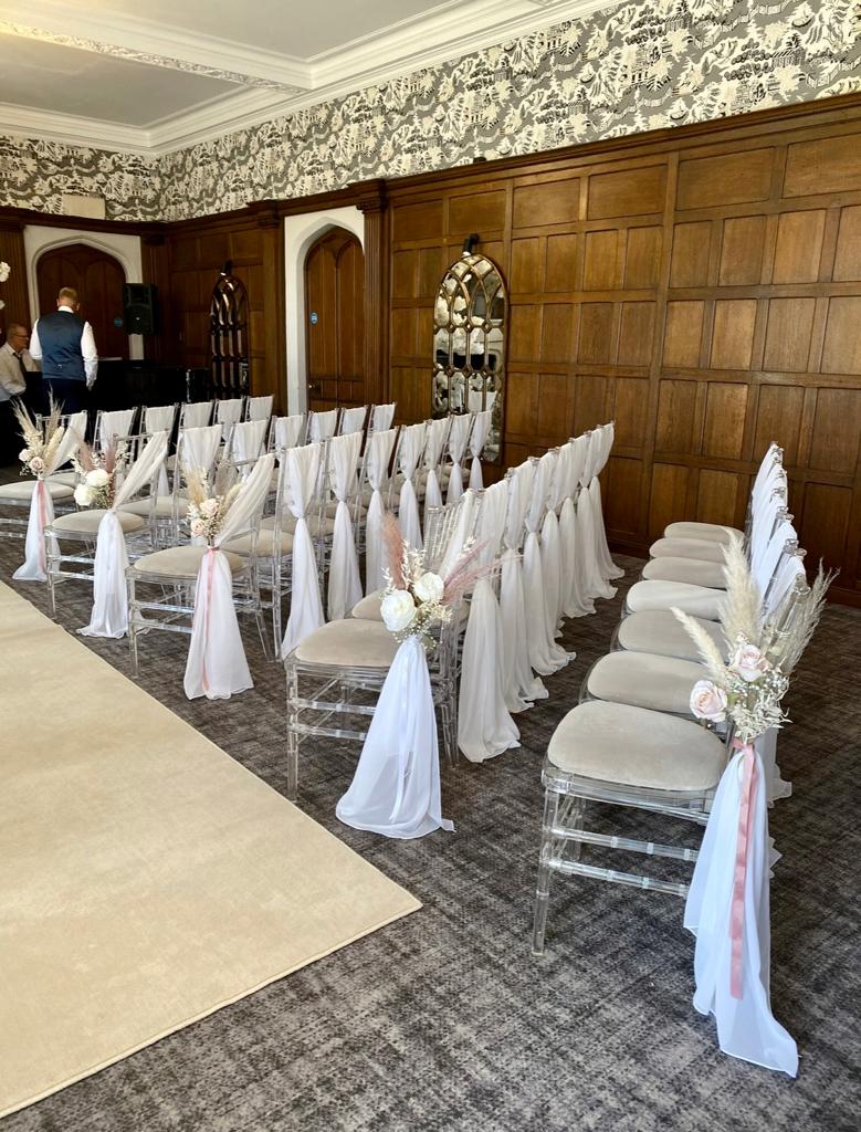 A row of clear chairs with white flowers on the backs