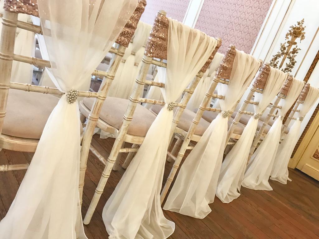 A row of chairs are decorated with white cloth and gold sequins