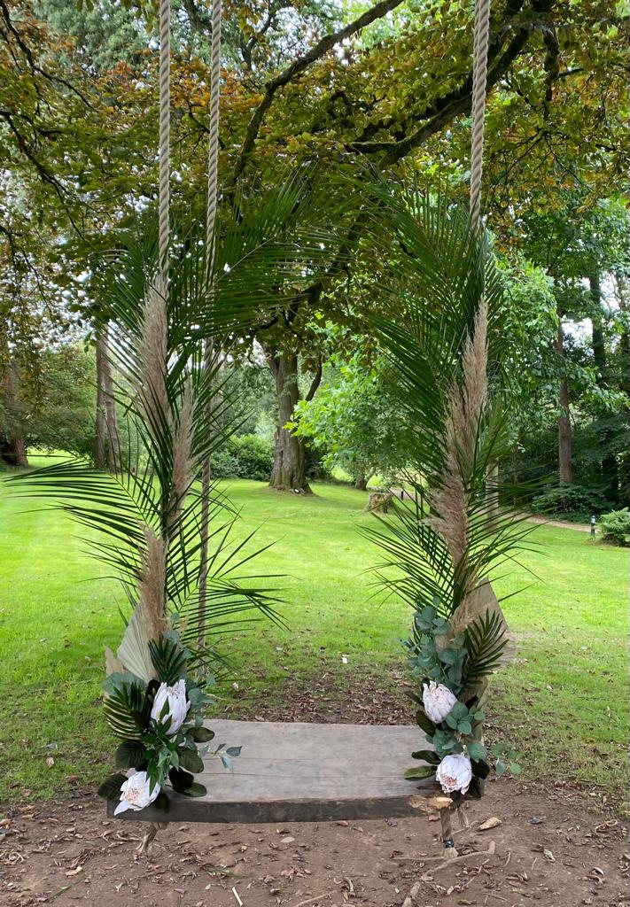 A rope swing decorated with palm leaves and flowers in a park