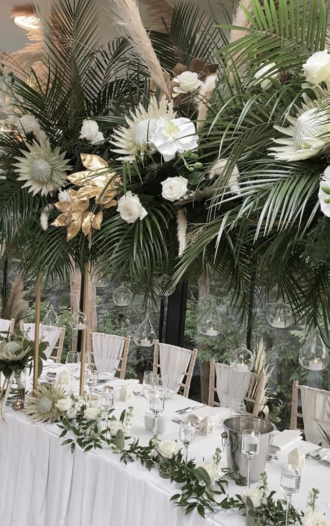 A table set for a wedding reception with white flowers and green leaves