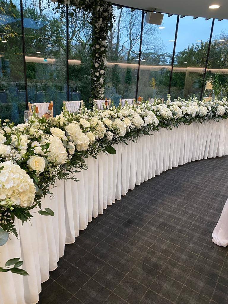 A long table with white flowers on it in front of a window