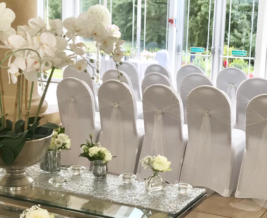 A row of white chairs with flowers and candles on a table