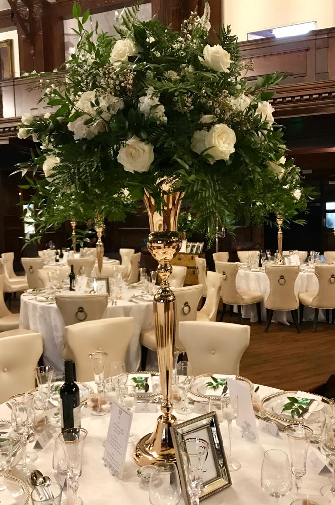 A large gold vase filled with white roses sits on a table
