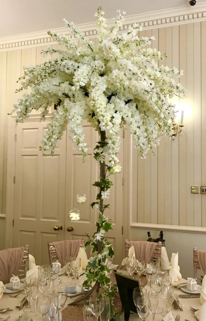 A tall tree filled with white flowers is sitting on a table
