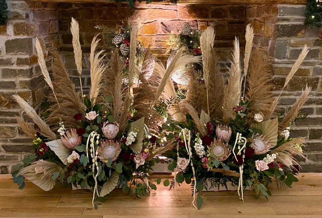 A fireplace decorated with flowers and pampas grass