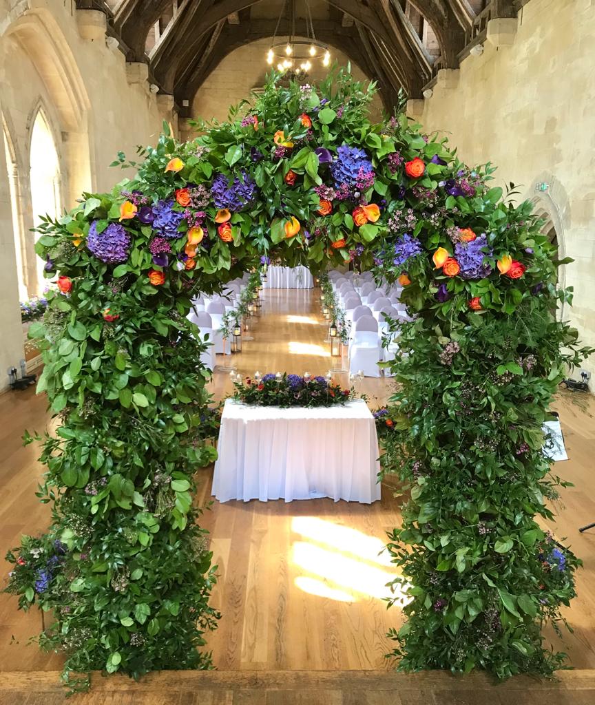 A large arch with purple and orange flowers surrounding a table