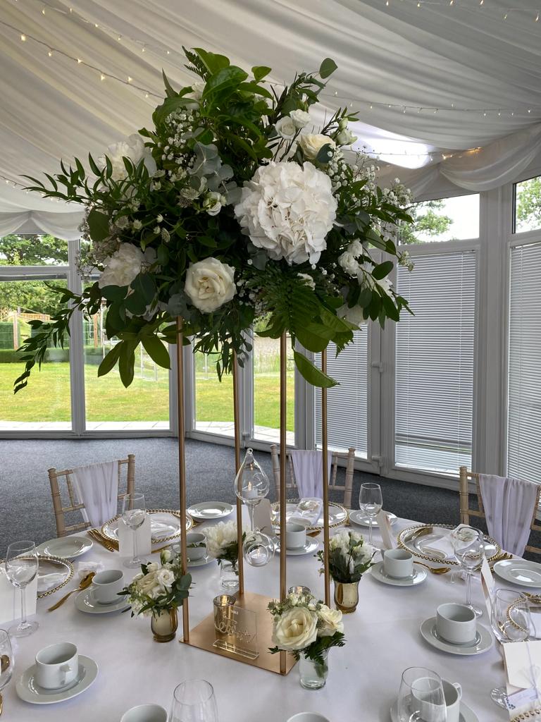 A table set for a wedding reception with white flowers and greenery on it
