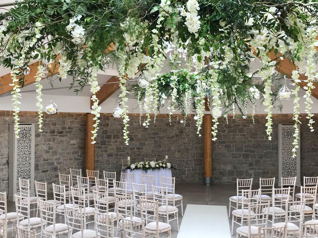 White chairs are lined up in a room with flowers hanging from the ceiling