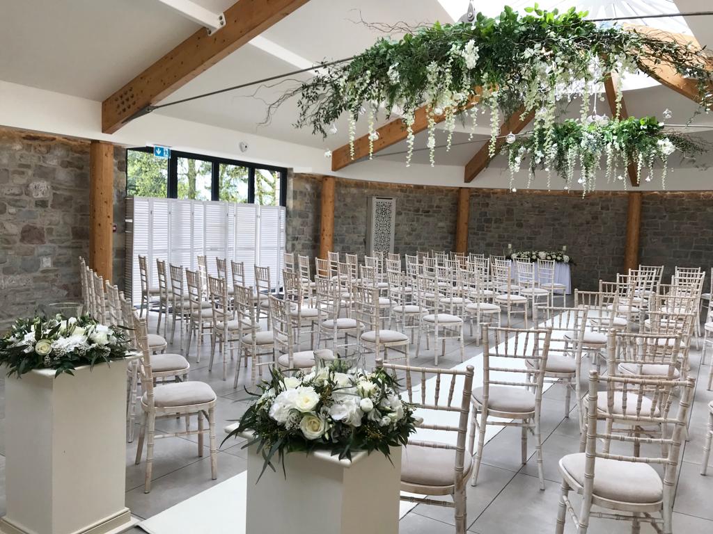 Rows of white chairs are lined up in a room with flowers hanging from the ceiling