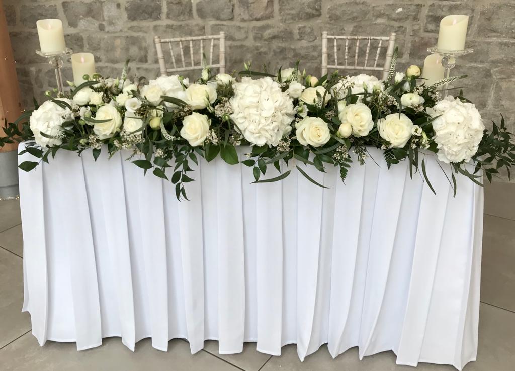 A long white table with white flowers and candles on it