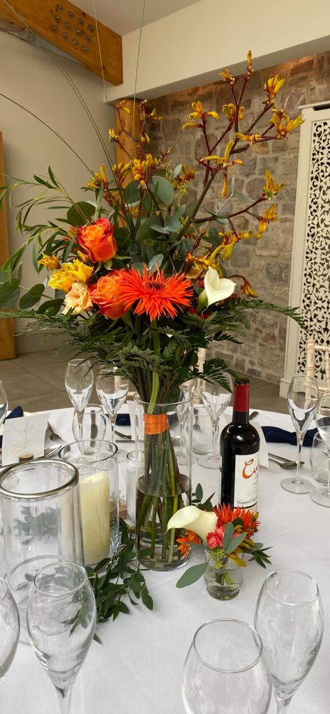 A bottle of cabernet wine sits on a table next to a vase of flowers