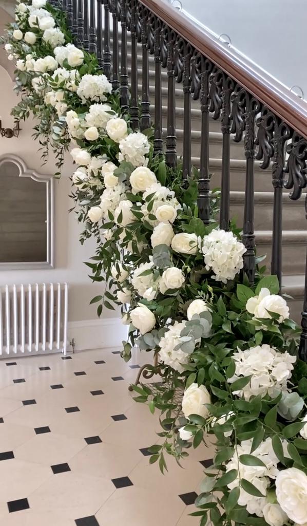 A staircase is decorated with white flowers and greenery