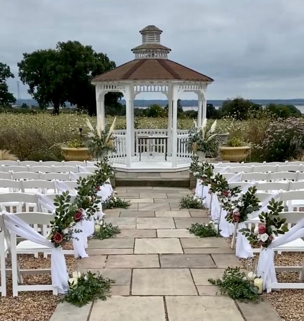 A white gazebo is decorated with flowers and candles for a wedding ceremony