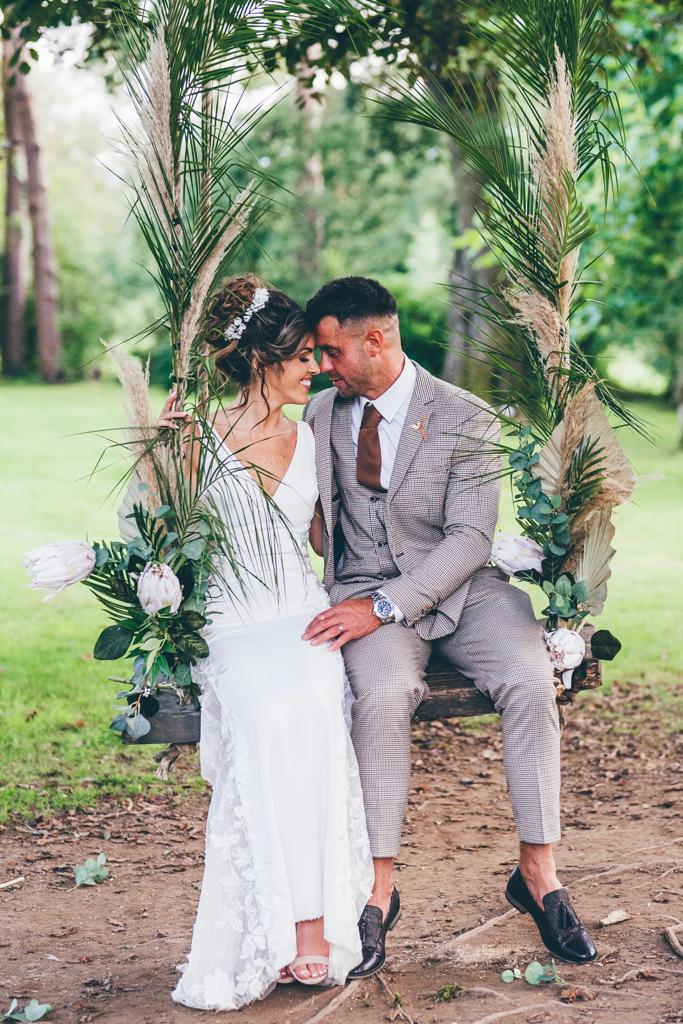 a bride and groom are sitting on a swing in a field