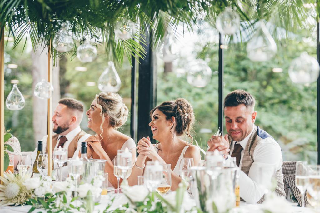 a bride and groom are sitting at a long table with their friends