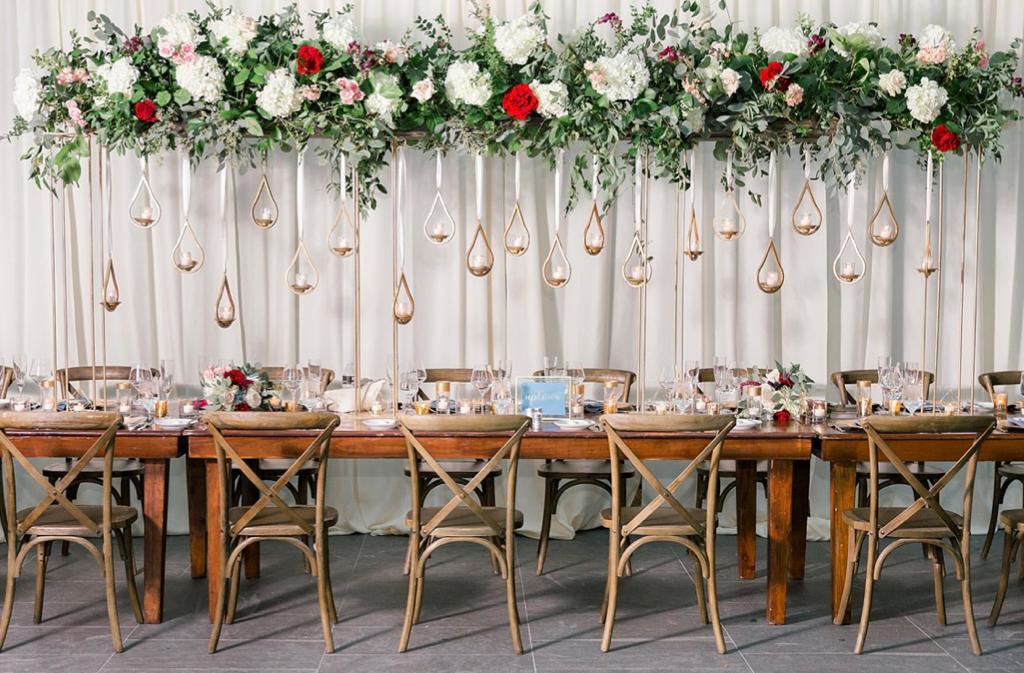 a long wooden table with cross back chairs and flowers hanging from the ceiling