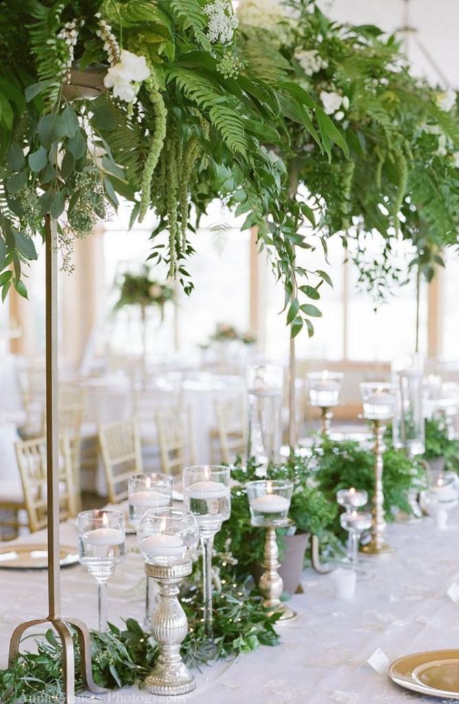 a table with candles and ferns hanging from the ceiling