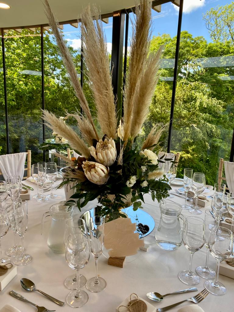a table set for a wedding reception with pampas grass and flowers on it