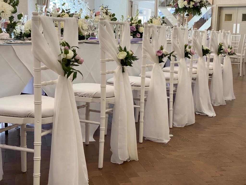 a row of white chairs are decorated with flowers