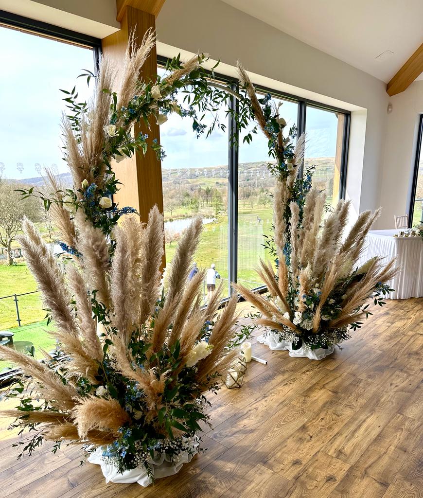 a room filled with flowers and pampas grass in front of a large window