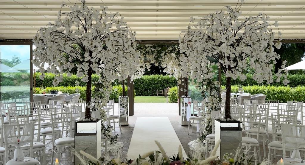 a wedding ceremony is taking place in a room with white chairs and trees decorated with white flowers