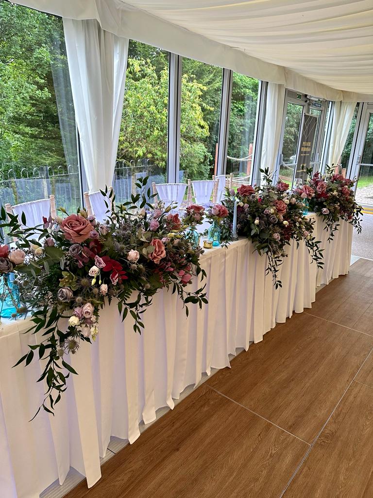 a long table with flowers on it in front of a large window