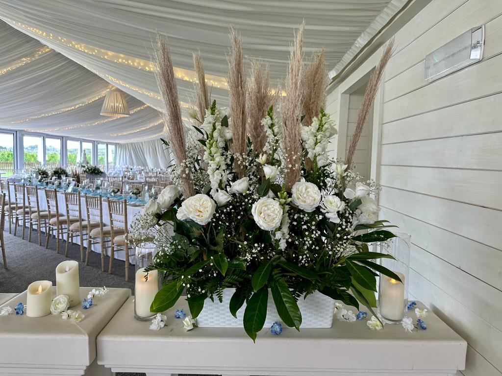 a vase filled with white flowers and pampas grass sits on a table