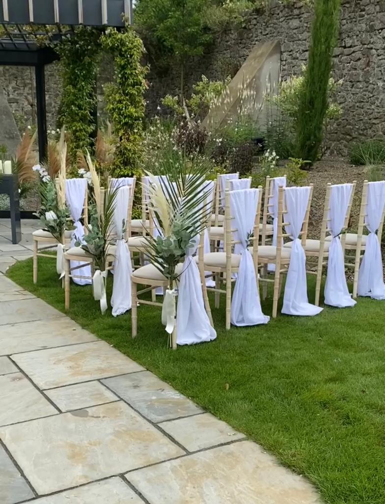a row of chairs are decorated with white cloths and leaves