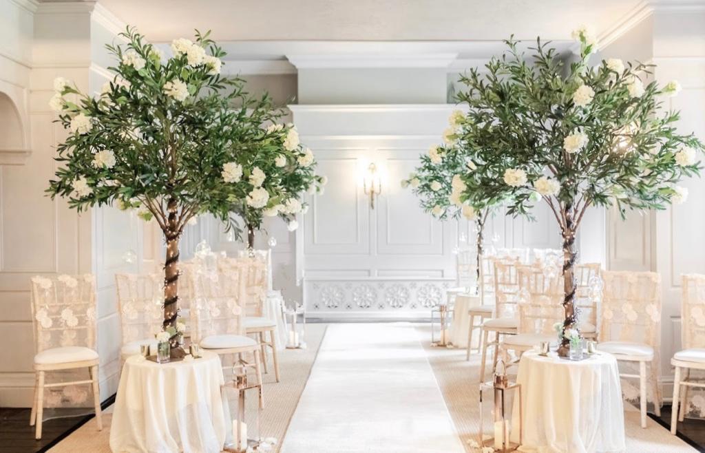 a wedding ceremony is taking place in a room decorated with white flowers and trees