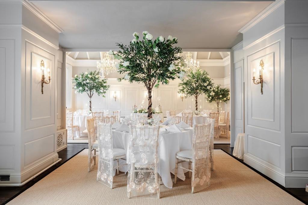a room with white tables and chairs and trees in the middle