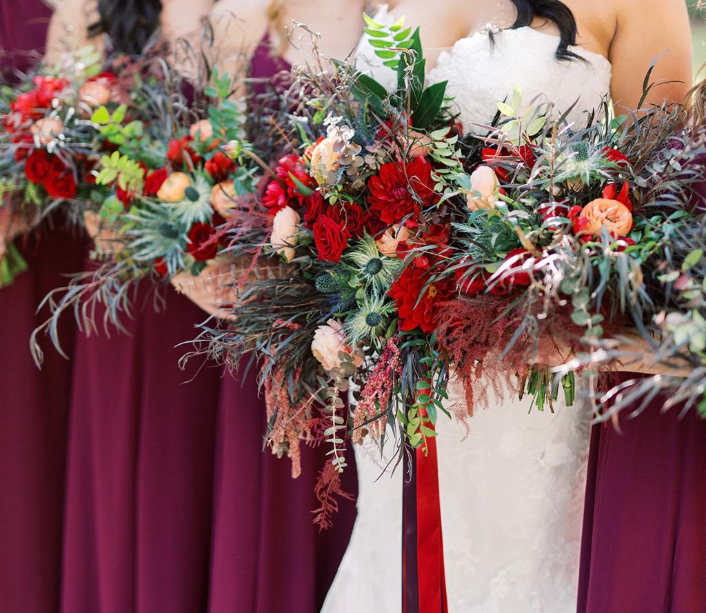 a bride and her bridesmaids hold bouquets of red flowers