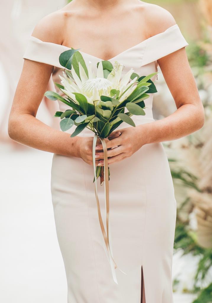 a woman in a white off the shoulder dress holds a bouquet of flowers