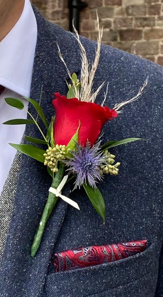 a man in a suit has a red rose buttonhole in his pocket
