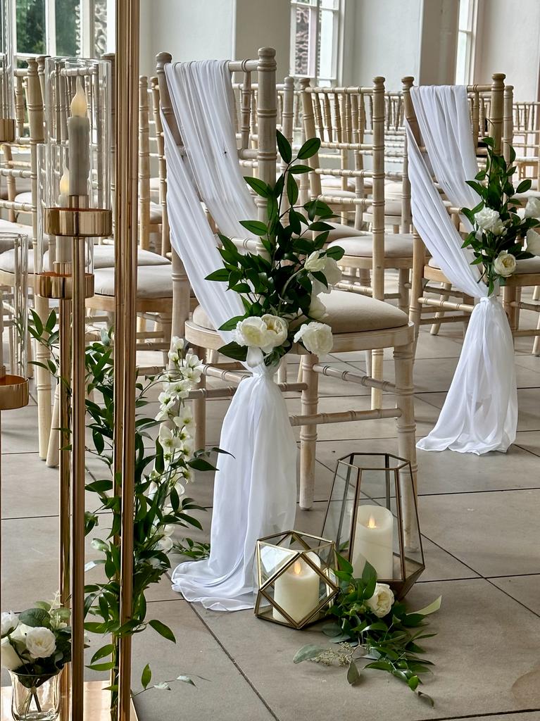 a row of chairs with white flowers and candles