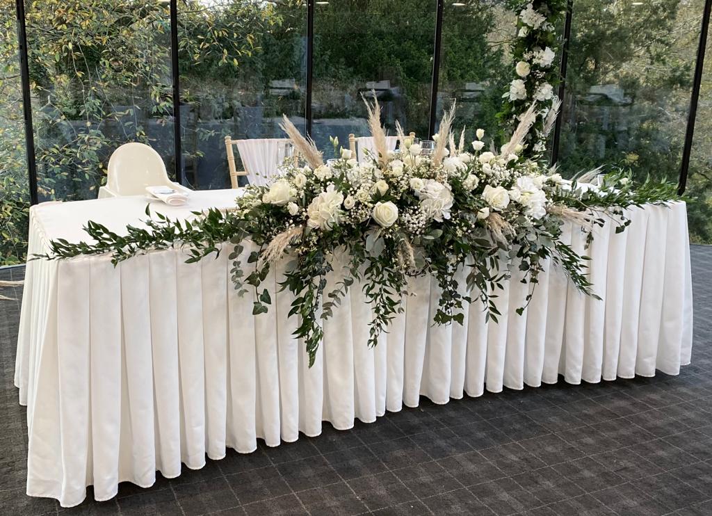 a long white table with flowers and greenery on it