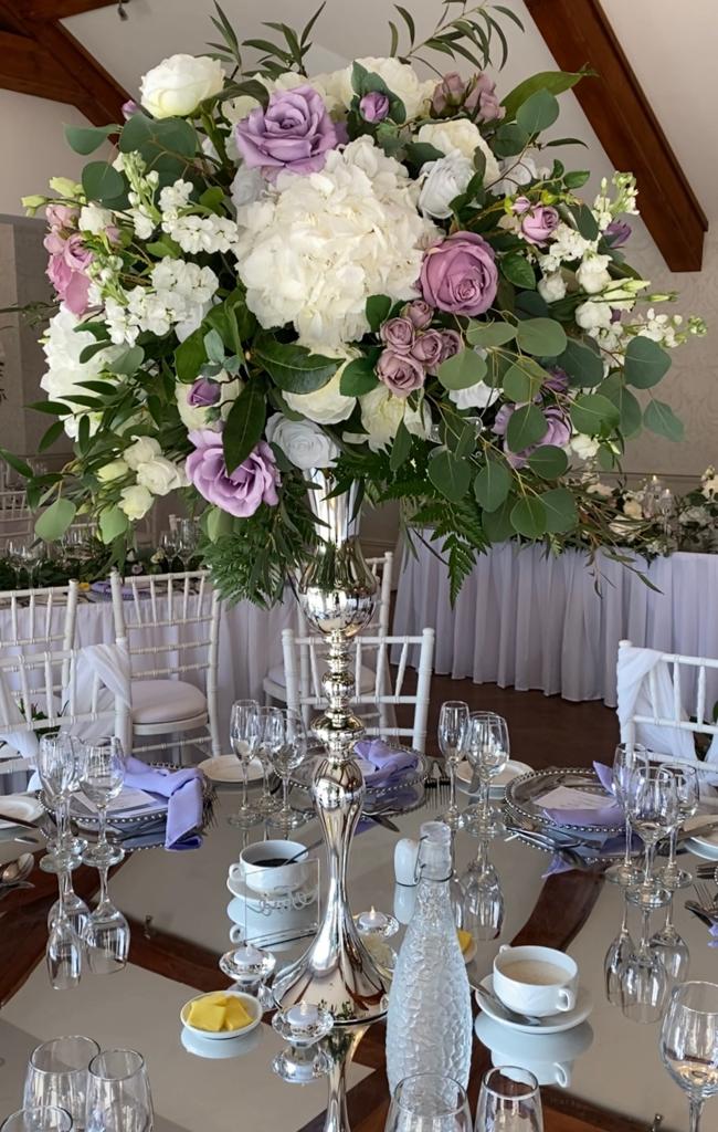 a silver vase filled with white and purple flowers sits on a table