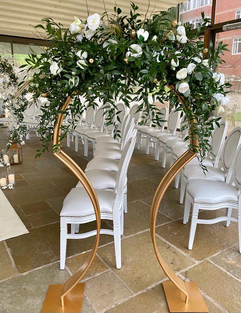 a row of white chairs are lined up in front of a gold arch with flowers in it